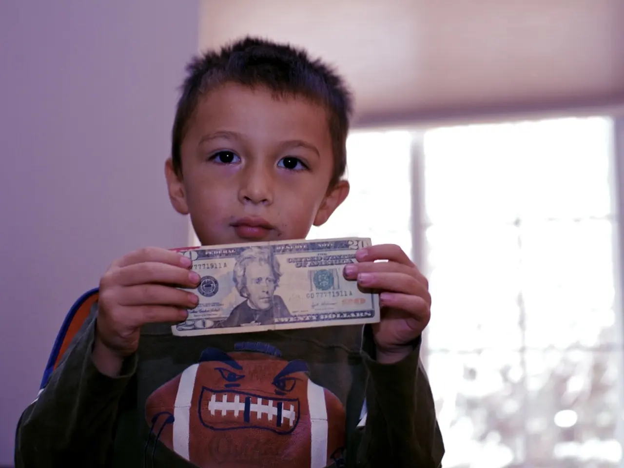 In this picture I can see there is a boy standing and he is holding money and there is a window in...
