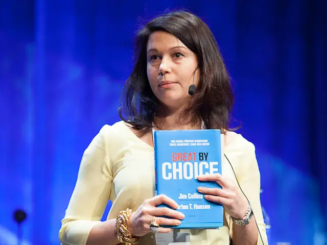 In the foreground of this image, there is a woman standing in cream dress holding a book in her...