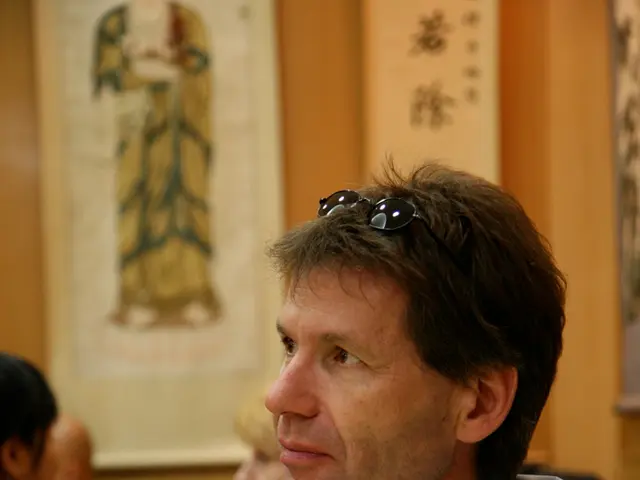 There is a man wearing light blue color shirt sitting and holding a cup. In front of him, there is...