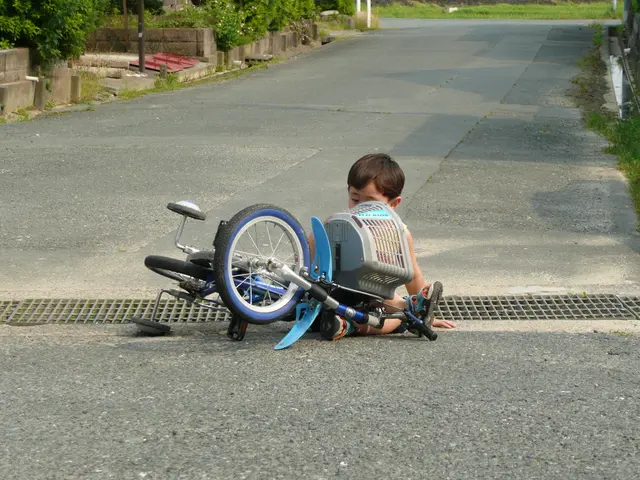 In this image we can see a kid sitting on the road and there is a bicycle. In the background there...